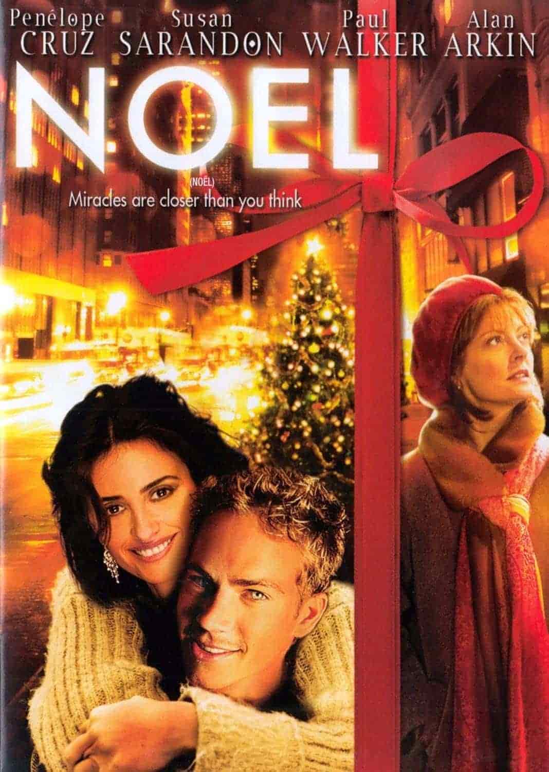 Movie poster for "Noel" featuring Penelope Cruz hugging Paul Walker, with Susan Sarandon standing to the right, a Christmas tree, and a red ribbon framing the image.