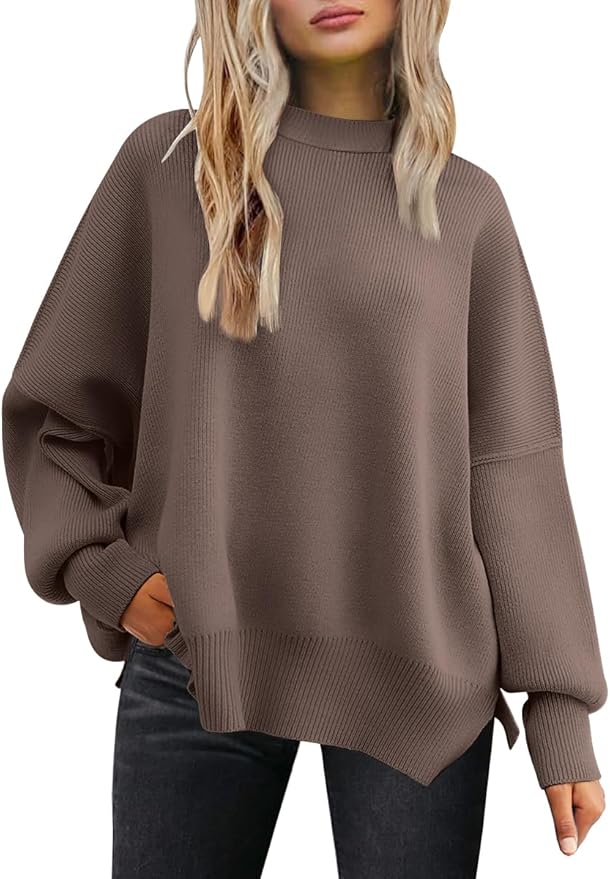 A woman wearing a loose-fitting, long-sleeve brown sweater and black jeans stands with one hand in her pocket.