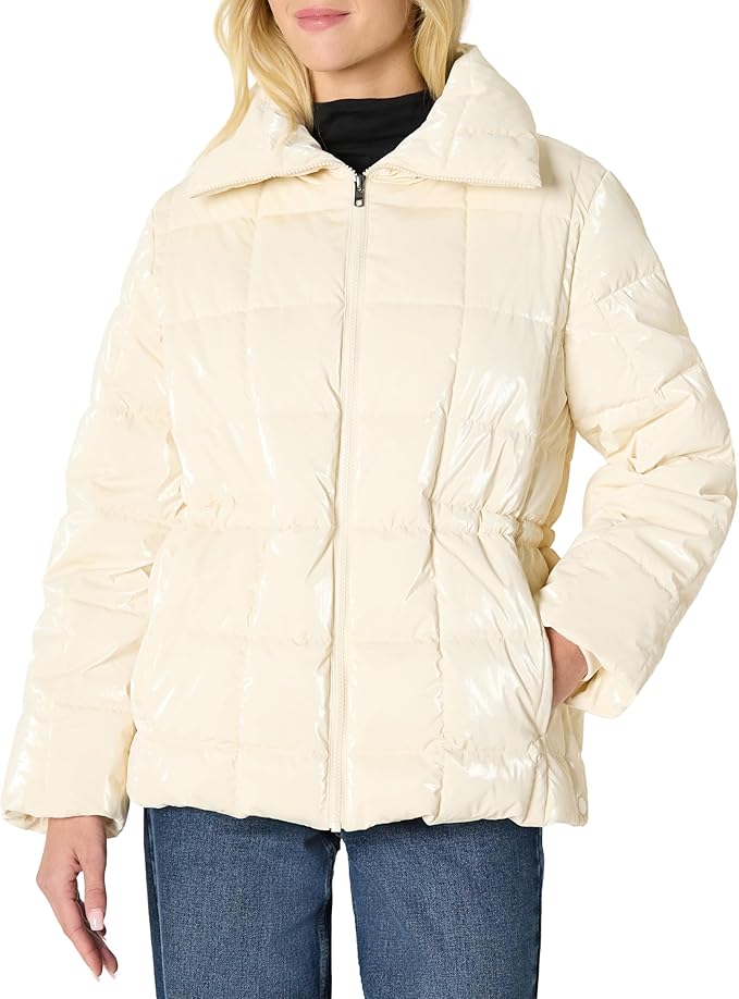 A person wearing a shiny off-white puffer jacket with a zipper front, standing with one hand in a pocket, paired with blue jeans.