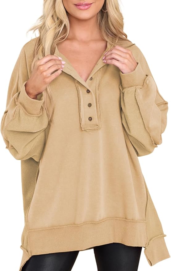 A woman wearing an oversized, tan, long-sleeve henley sweatshirt with a buttoned collar and black leggings.