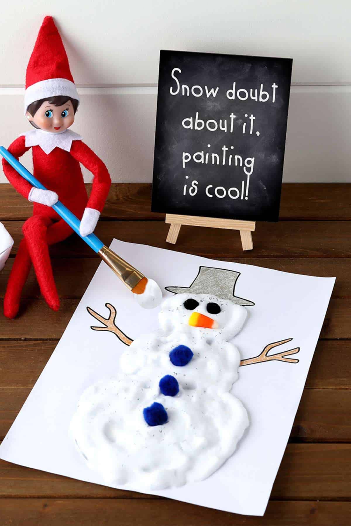 A felt elf doll holds a paintbrush next to a shaving cream snowman craft and a sign that reads, "Snow doubt about it, painting is cool!.