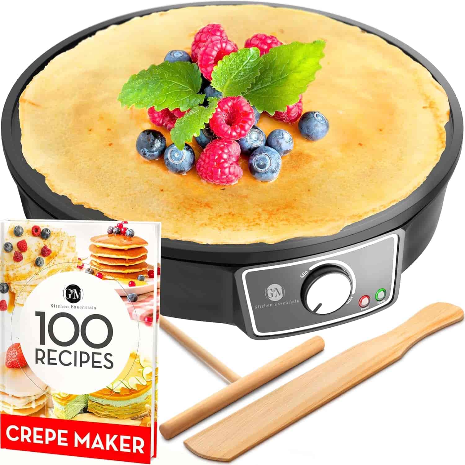 Electric crepe maker with a cooked crepe topped with berries and mint, accompanied by a recipe book and two wooden utensils.