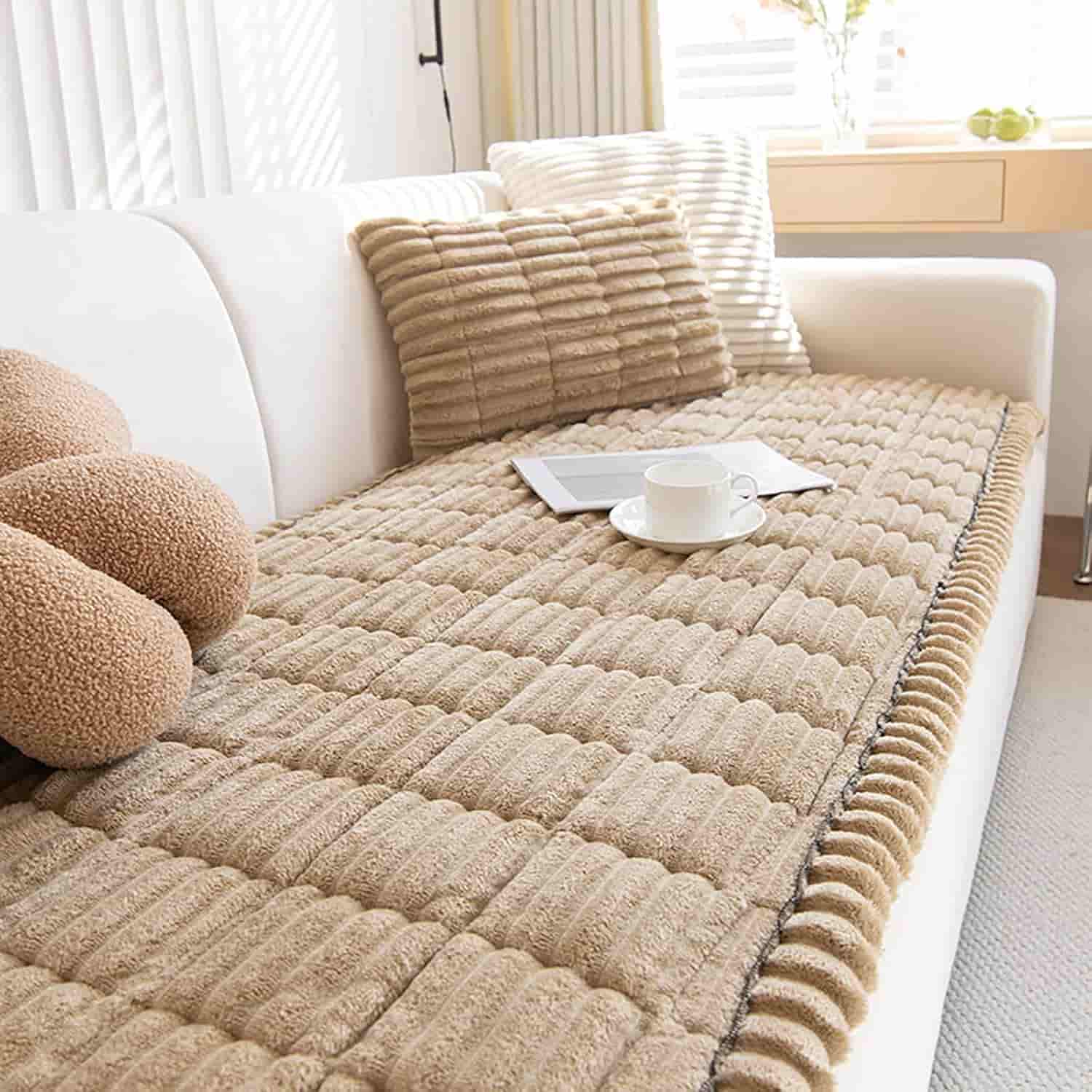 A beige textured sofa cover with matching cushions on a white couch, a cup and saucer, and sunlight coming through nearby windows.