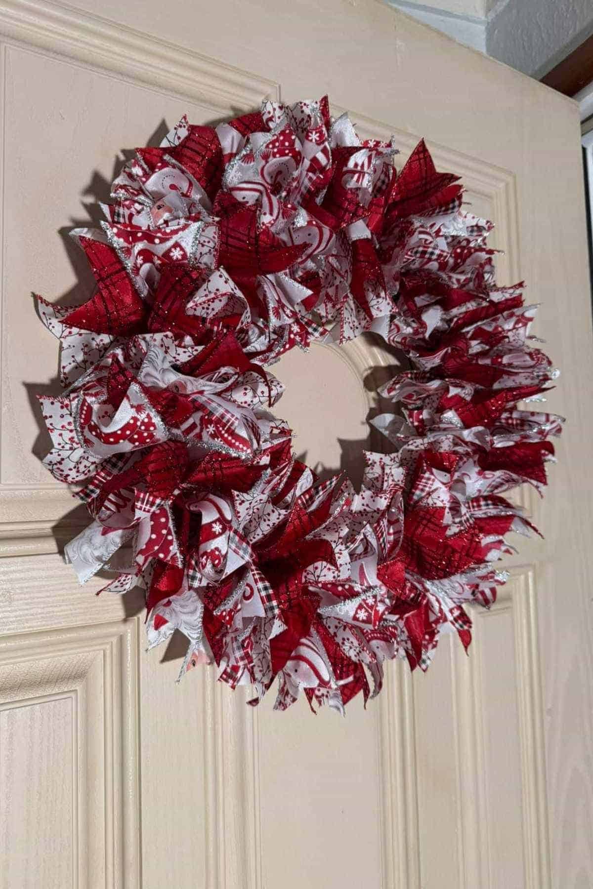 A wreath made of red and white patterned fabric pieces hangs on a light-colored door.