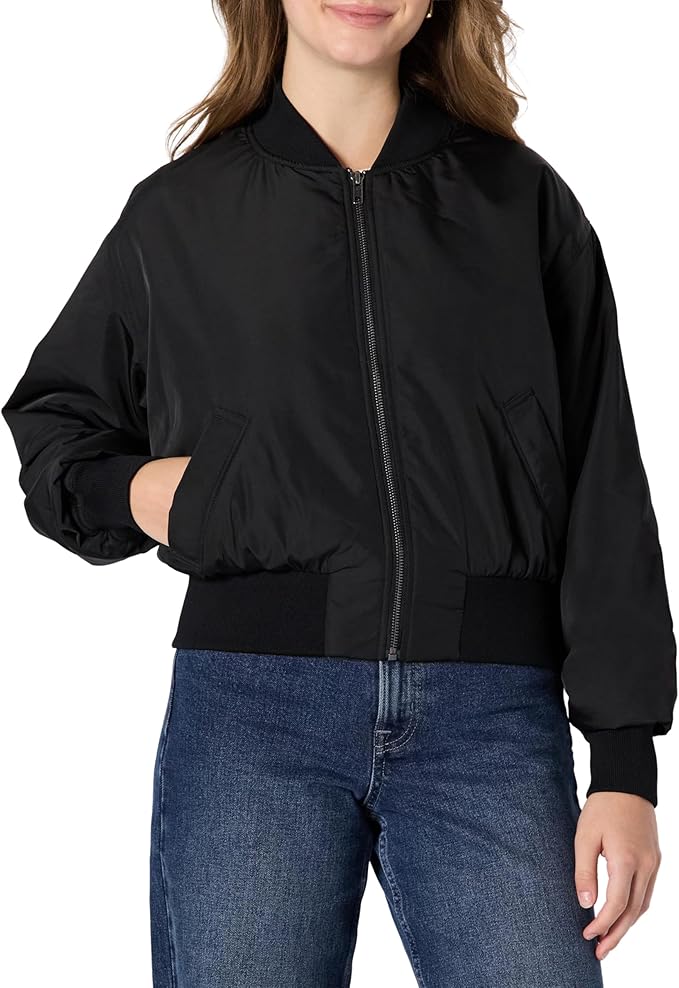 A person wearing a black zip-up bomber jacket with ribbed cuffs and waistband, paired with blue jeans, standing against a plain background.