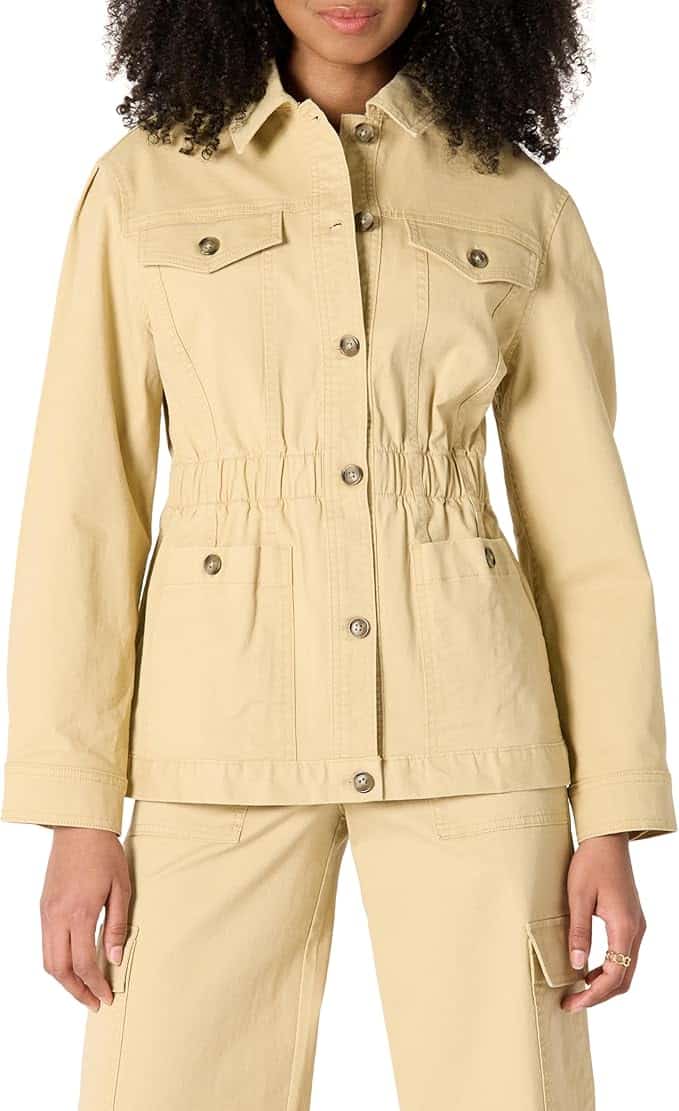 A person wearing a light beige utility jacket with button closures, chest and hip pockets, and matching beige pants.