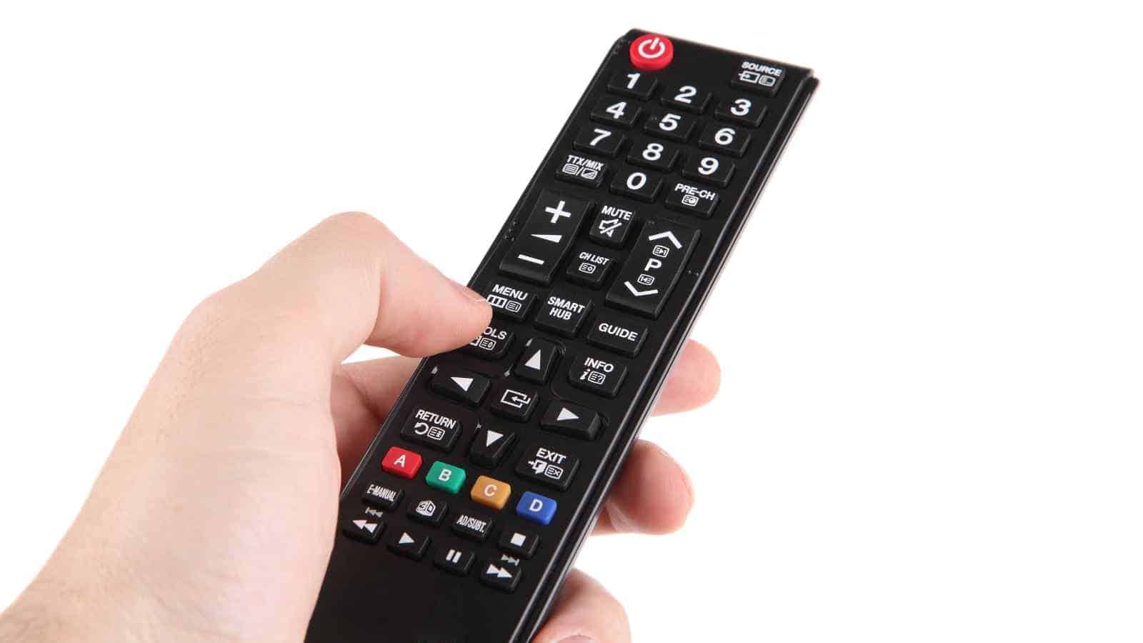 A hand holding a black TV remote control against a white background.