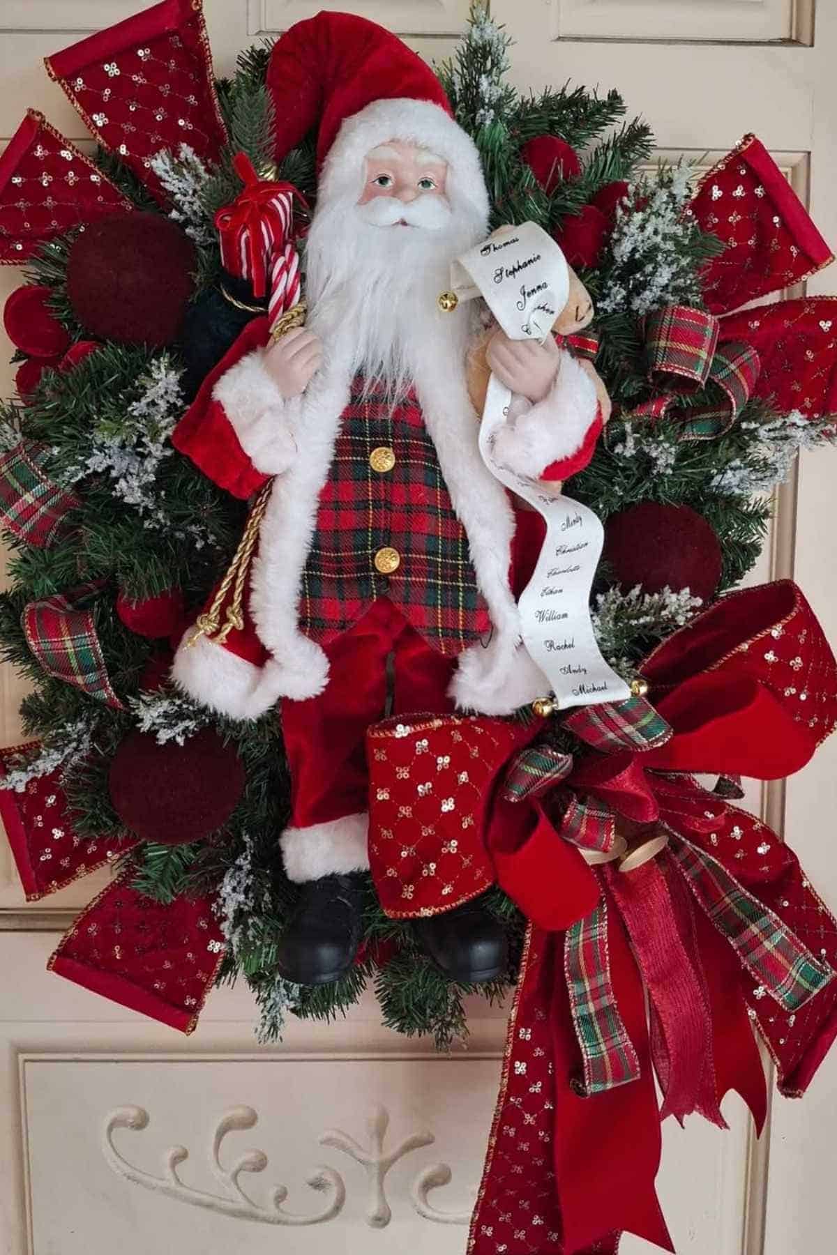 A Christmas wreath decorated with red bows, plaid ribbons, and a Santa Claus doll holding a list and candy cane.
