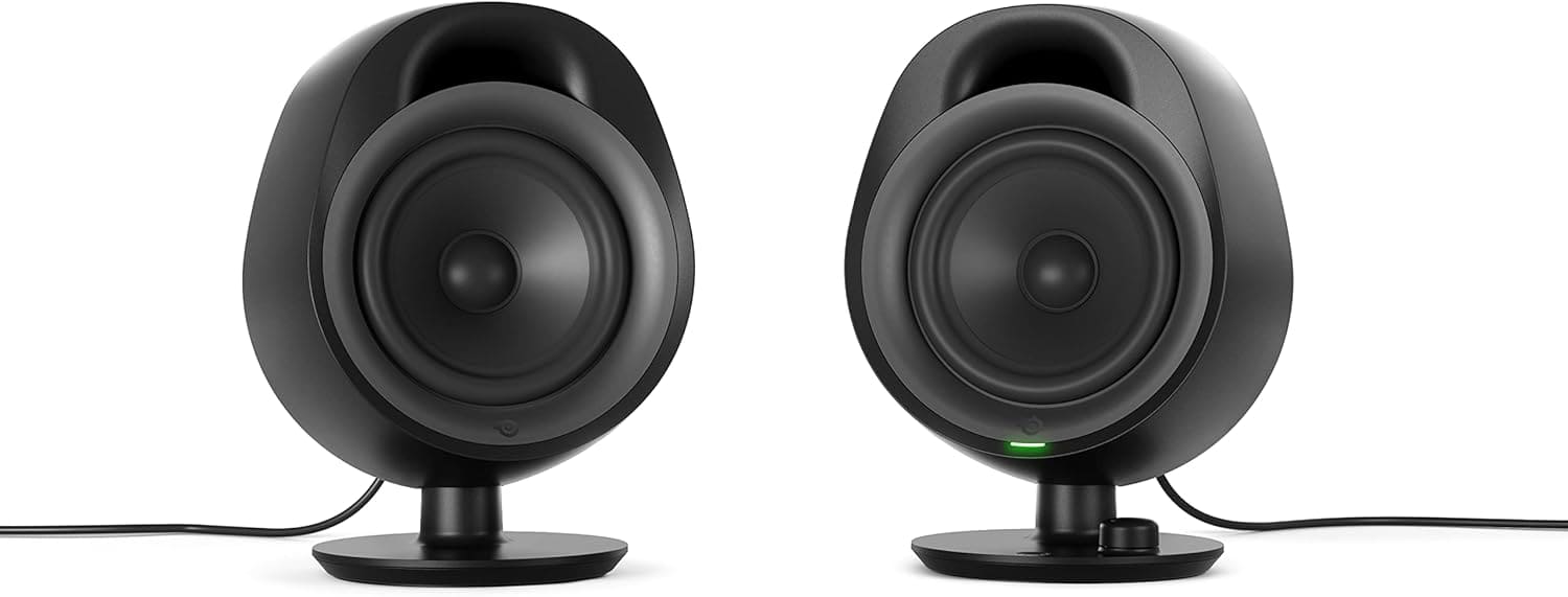 Two black, rounded desktop speakers on stands with visible power cords; the right speaker has a small green light and a control knob.