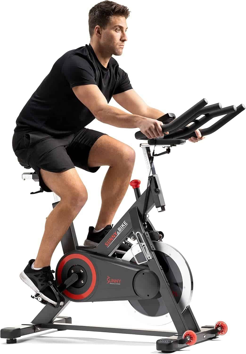 A man wearing black athletic clothing rides a stationary exercise bike indoors.