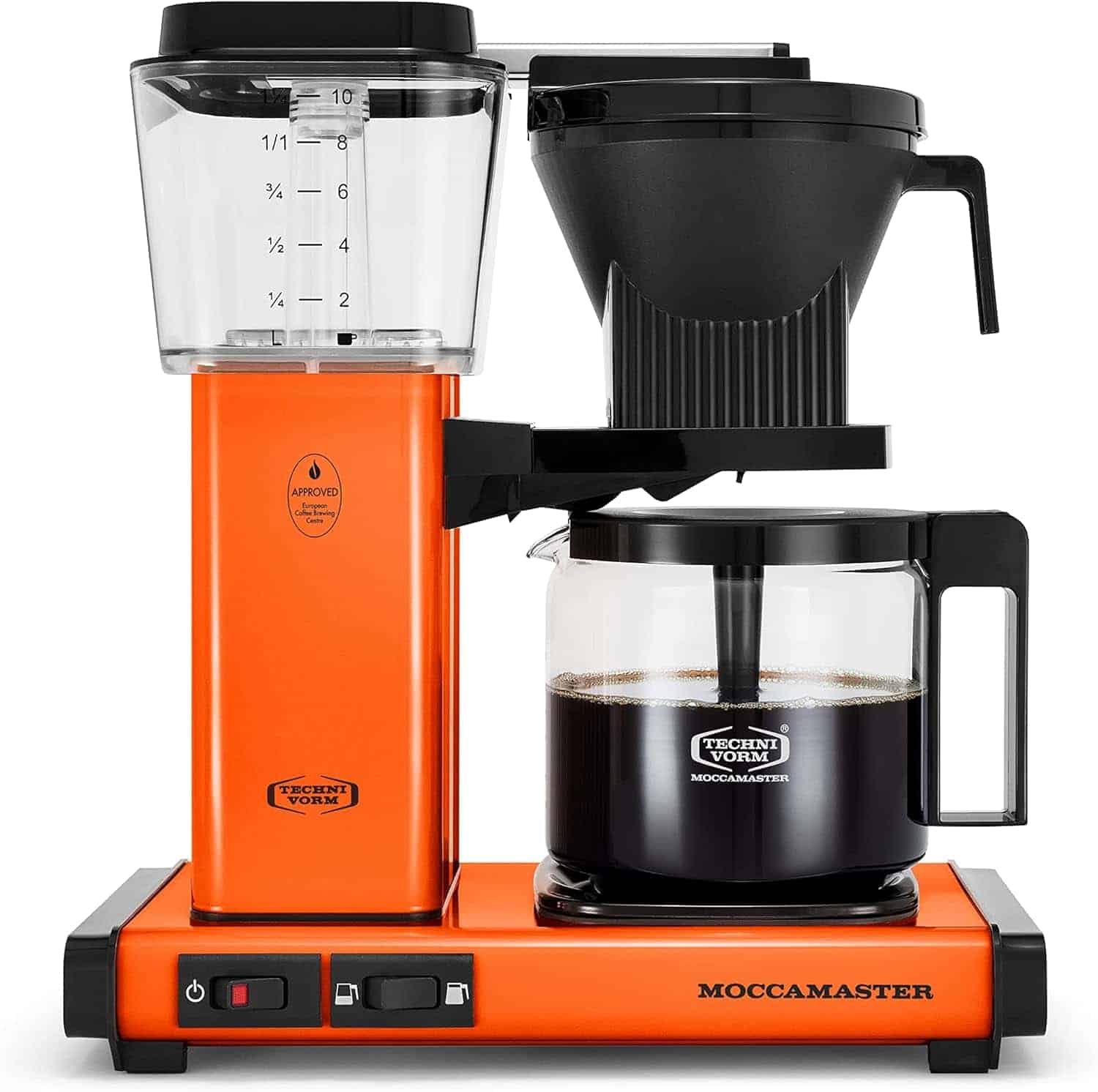 An orange Moccamaster coffee maker brews coffee into a glass carafe, with measurement markings visible on the water reservoir.