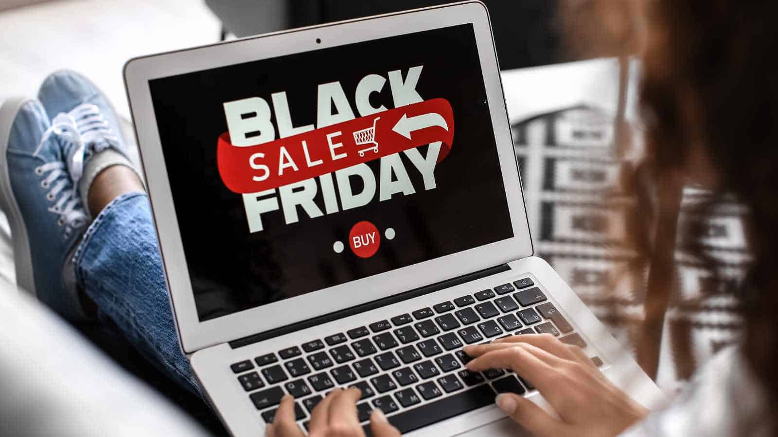 Person using a laptop showing a Black Friday sale advertisement on the screen, with a red "Buy" button visible.