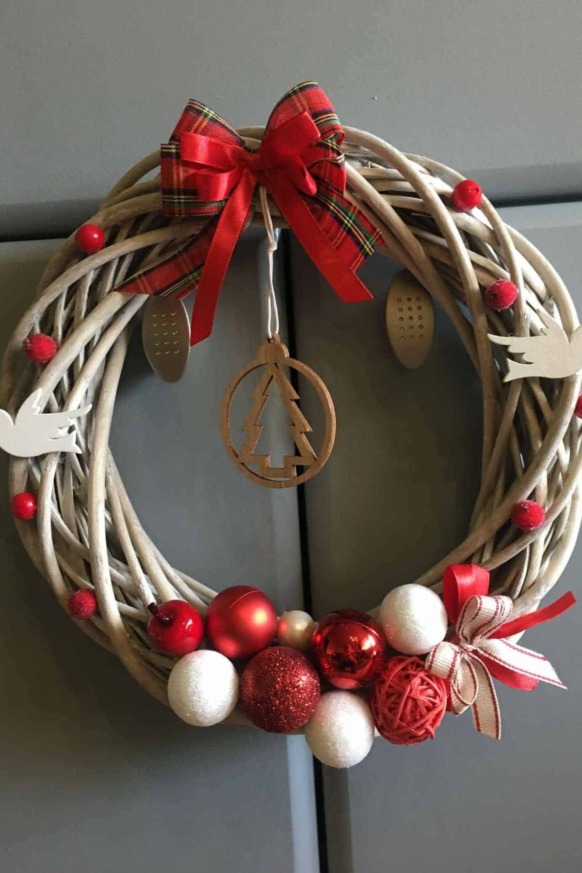 A decorative holiday wreath with red and white ornaments, red bows, small white birds, and a wooden tree ornament hanging in the center.