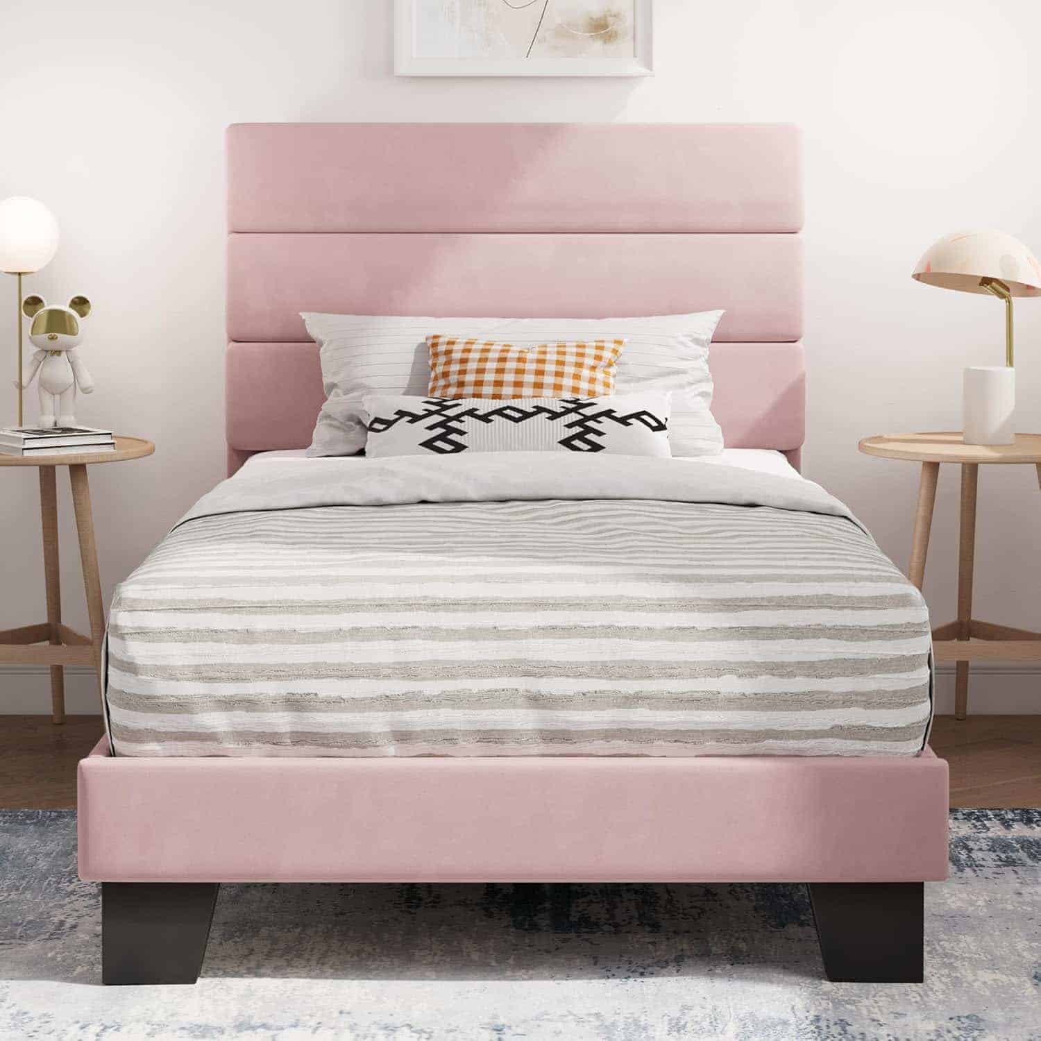 A neatly made bed with a pink upholstered headboard, striped bedding, and a checkered accent pillow, flanked by two round wooden nightstands with lamps.