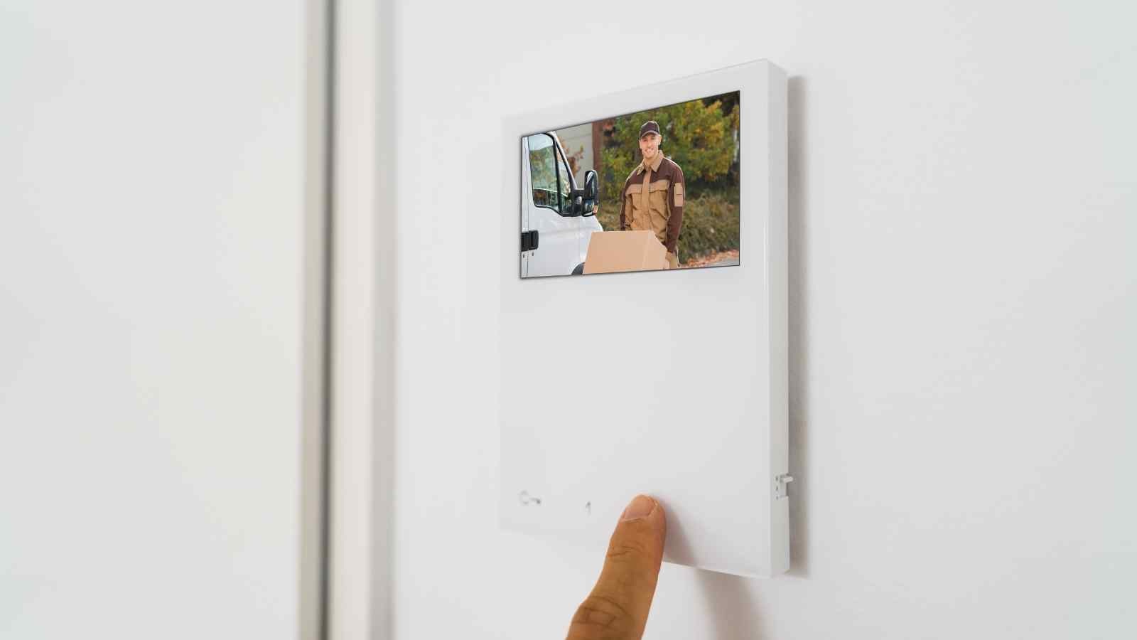 A person presses a button on a wall-mounted video intercom screen showing a delivery person standing outside with a package.