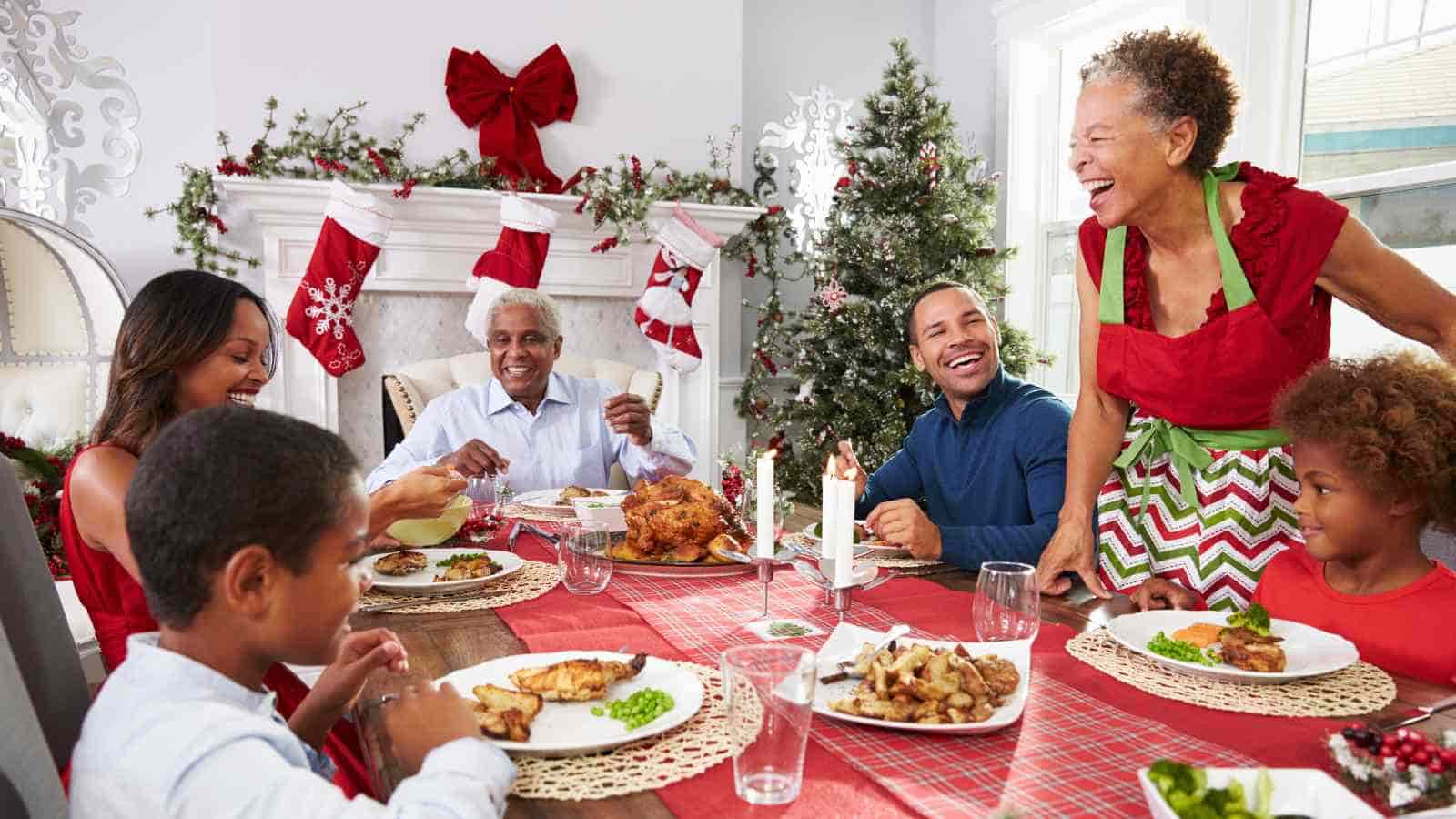 A family of five shares a festive meal at a table decorated for Christmas with a tree and stockings in the background.