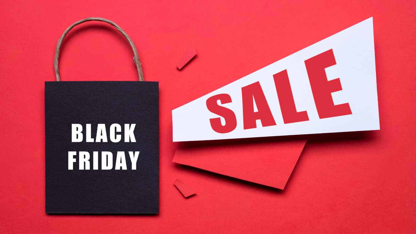 A black shopping bag labeled "Black Friday" next to a white sign with large red "SALE" text on a red background.