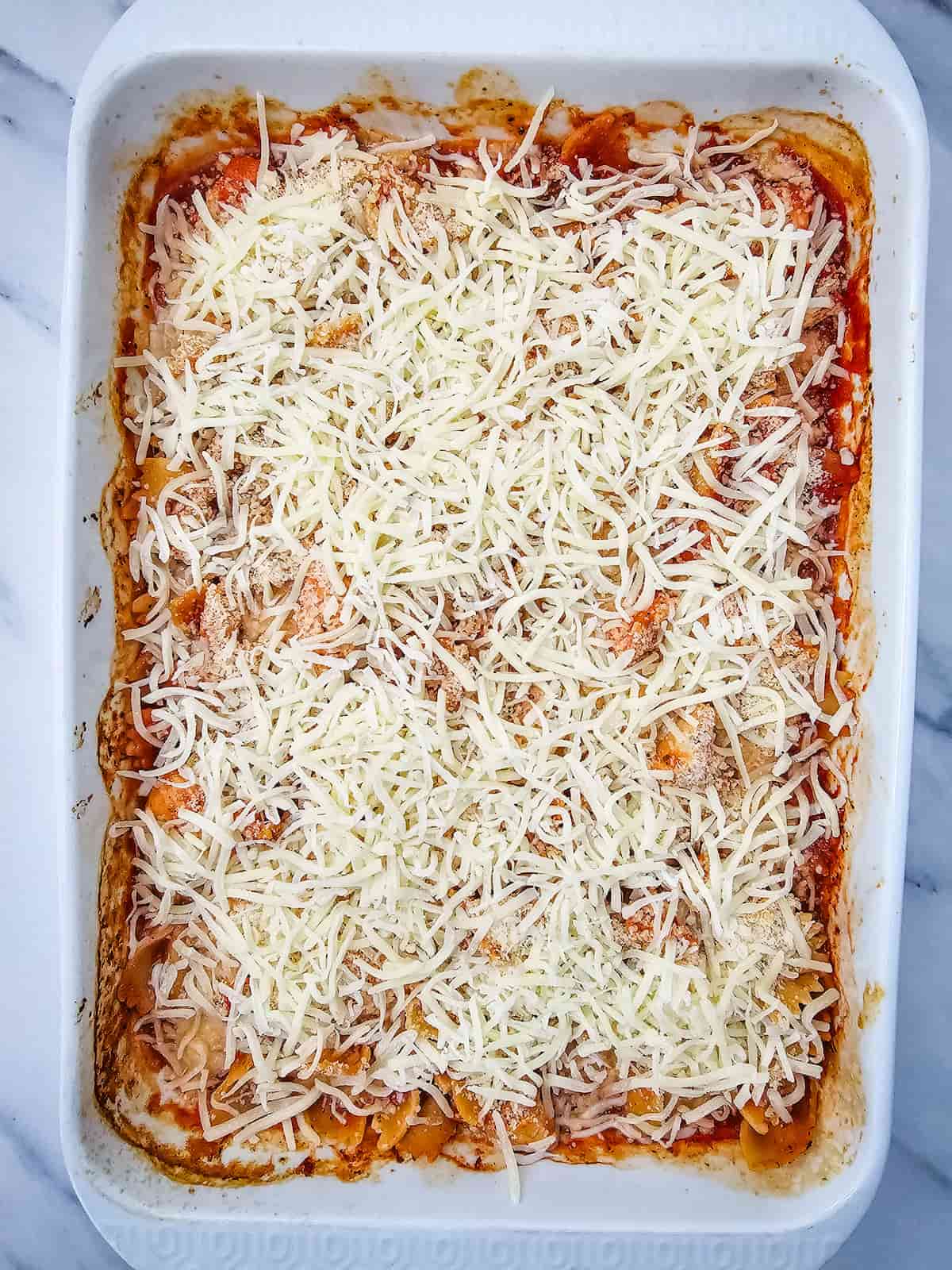 A rectangular baking dish filled with pasta, sauce, and topped with a layer of shredded cheese.