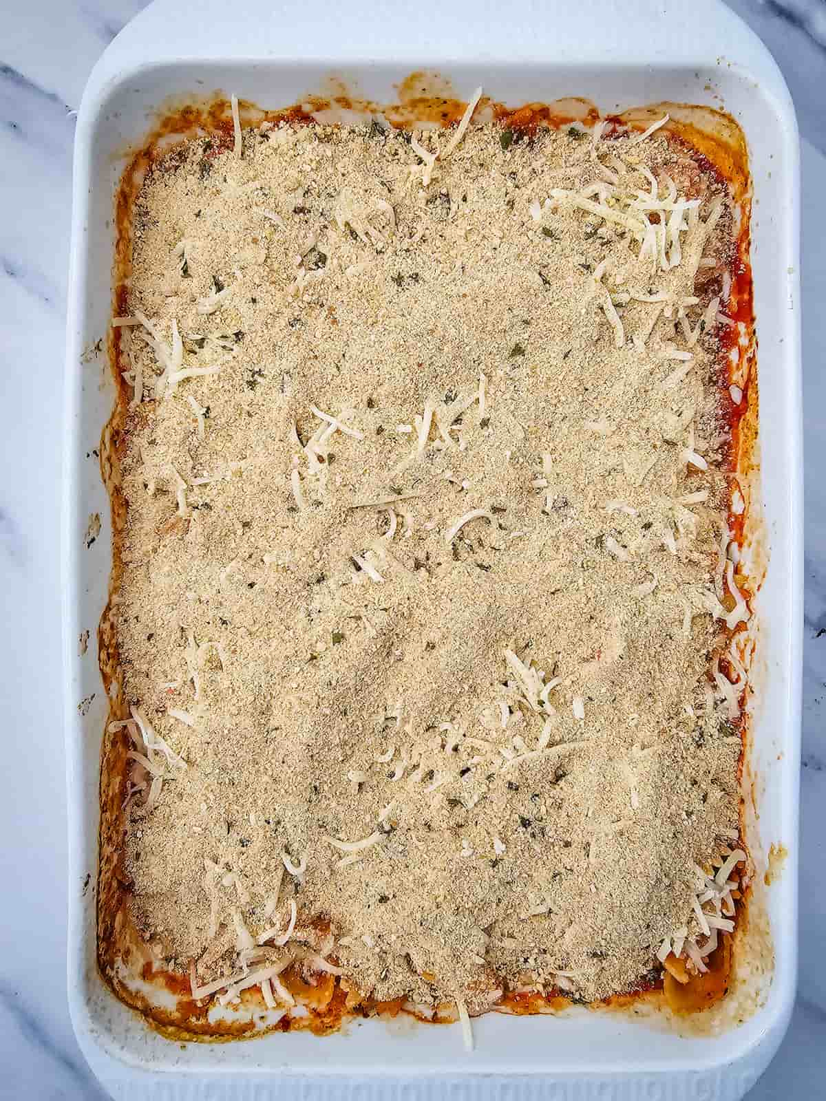 A baking dish filled with pasta topped with breadcrumbs and shredded cheese, ready to be baked.