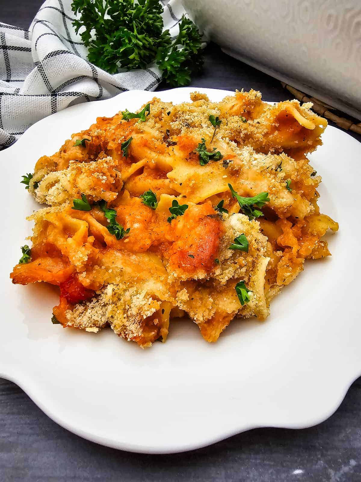 A serving of baked pasta with breadcrumb topping and garnished with fresh parsley on a white plate.