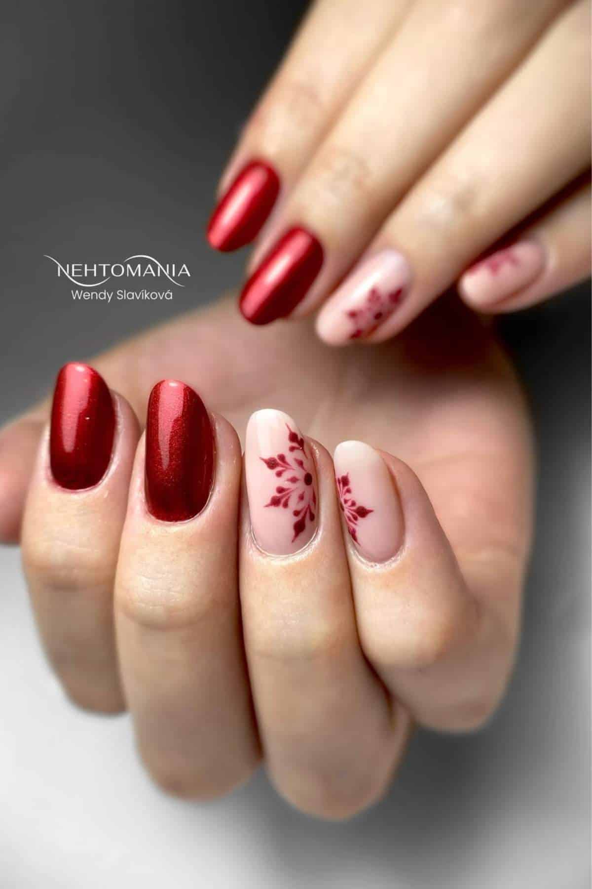 A hand with manicured nails featuring red polish and accent nails with matte nude polish and red floral designs.