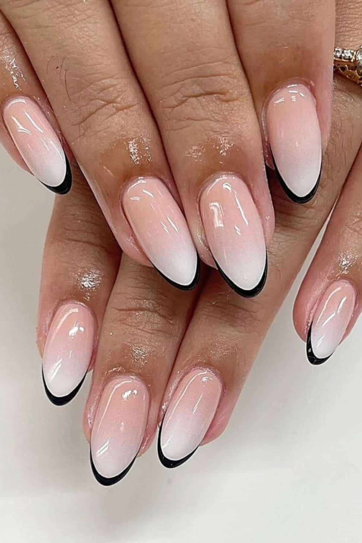 Hands with almond-shaped nails featuring a pink ombre base and thin black French tips.