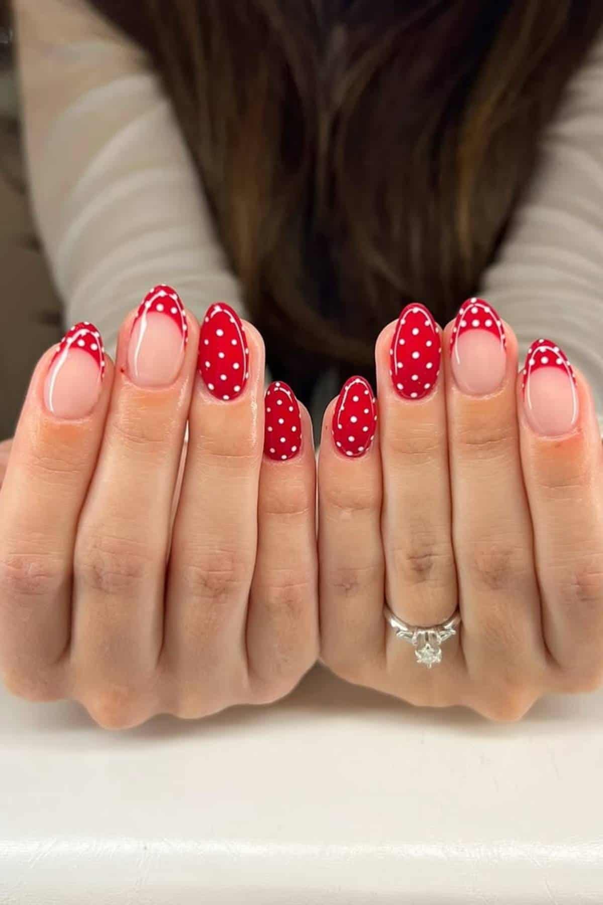 Close-up of hands with long nails featuring red tips and white polka dots; person is wearing a silver ring with a star-shaped design on one finger.