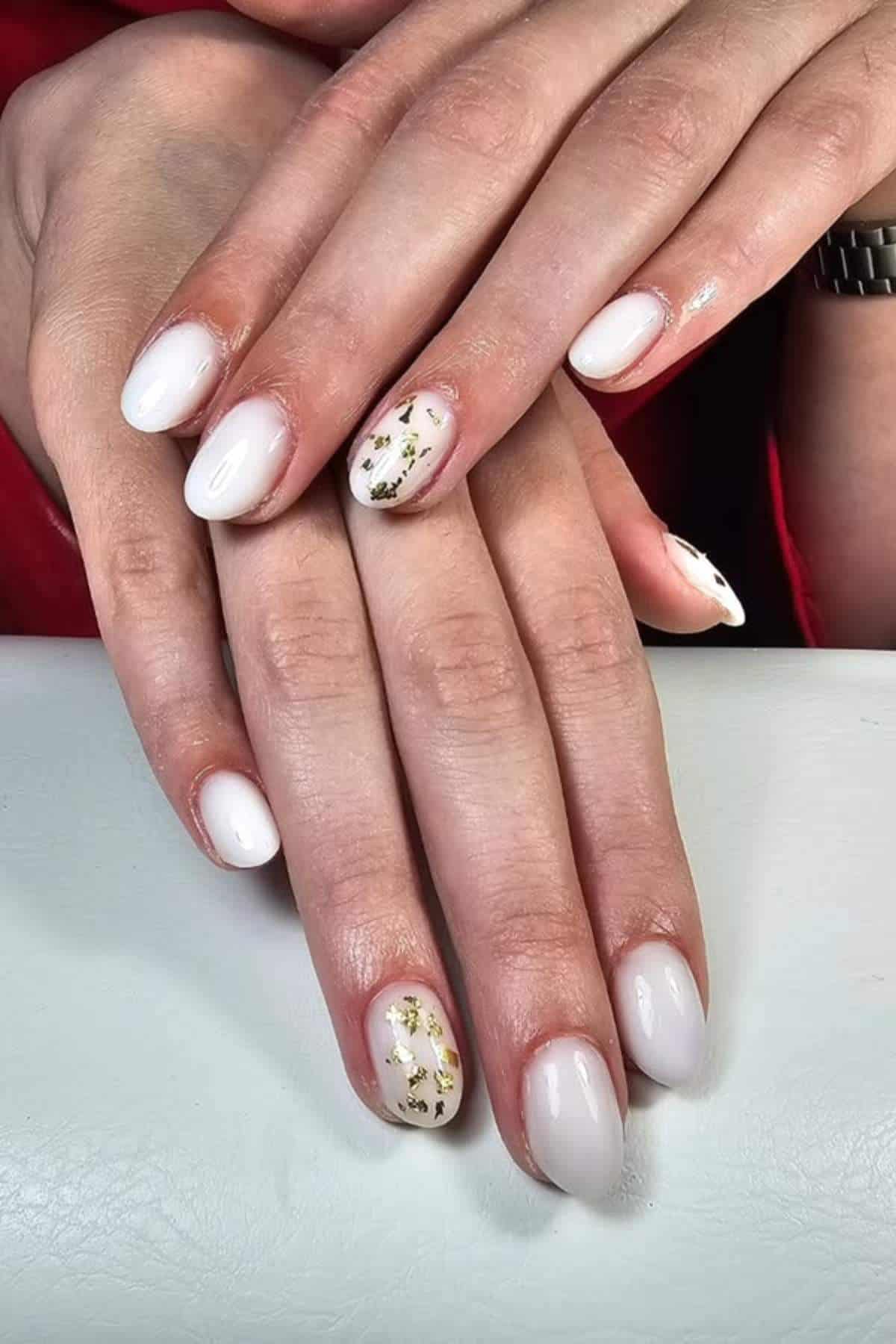 Close-up of hands with short, rounded nails painted white; accent nails feature gold foil details.