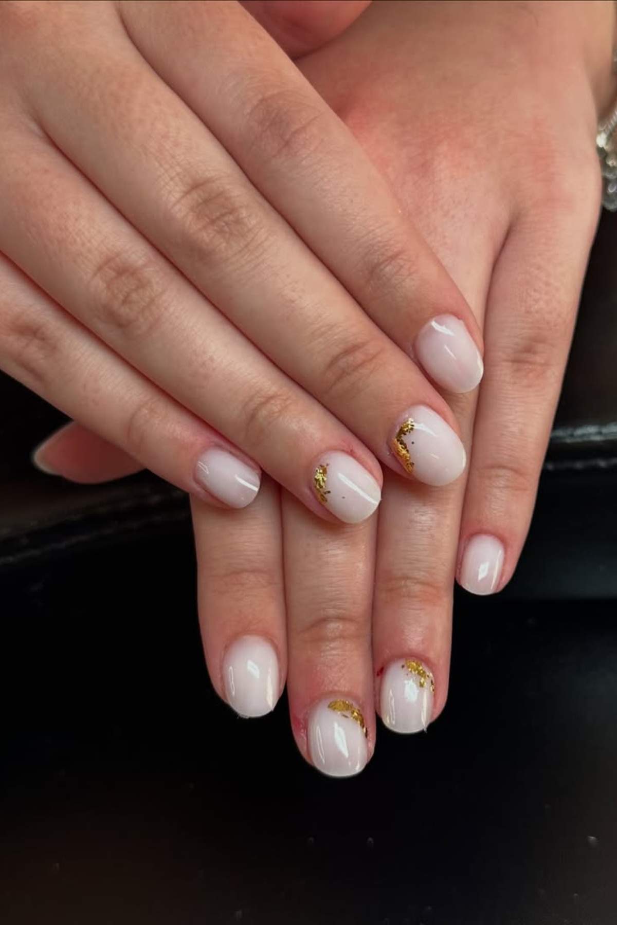 Hands with short, oval-shaped nails painted pale pink, featuring small gold foil accents on the ring and thumb nails.