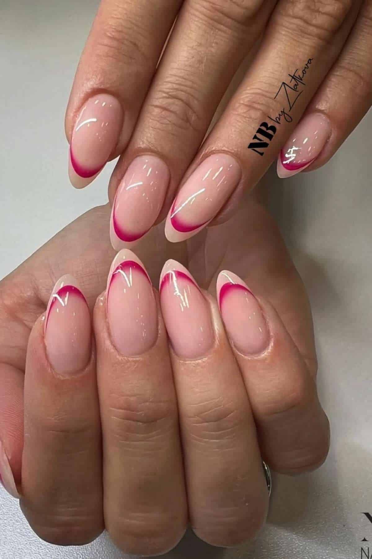 Hands with almond-shaped nails featuring a natural base and hot pink French tips, with some tips outlined in white.