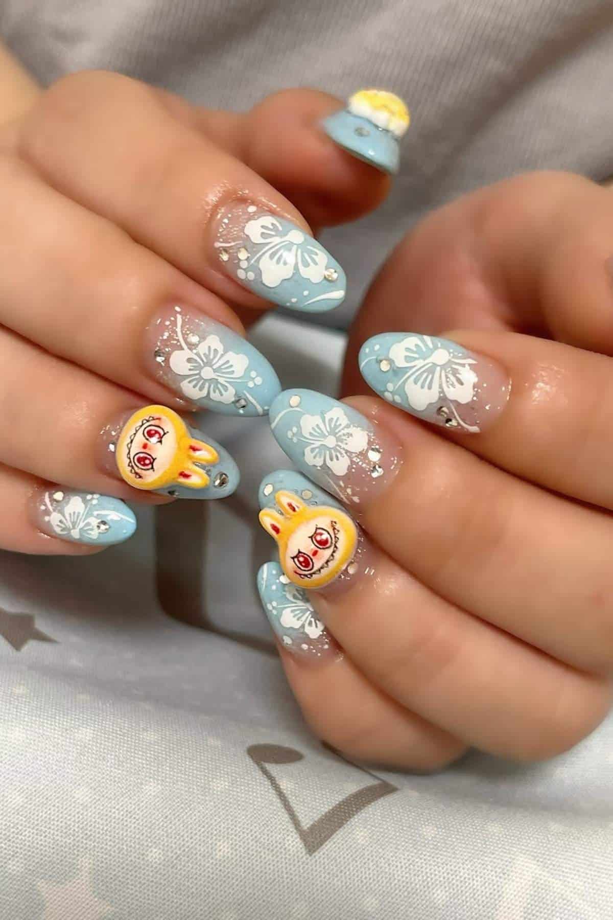 A pair of hands with blue, floral nail art and 3D cartoon rabbit decorations on some nails.