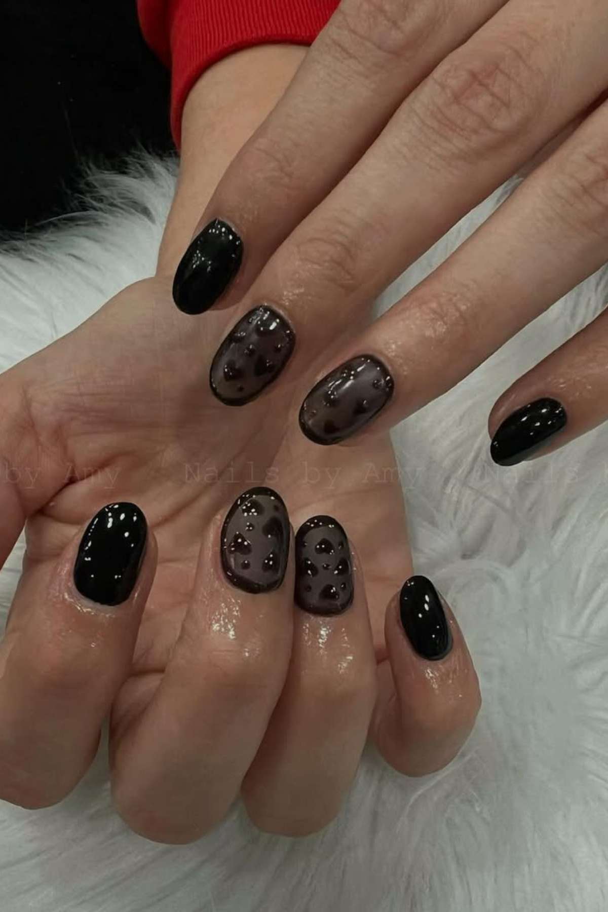 Close-up of hands with black and smoky gray gel nail polish, some nails decorated with small clear raised dots for a textured effect.