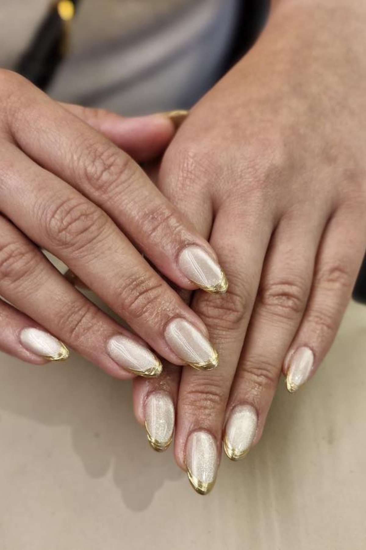 Close-up of hands with almond-shaped fingernails painted in a shimmery pale gold color and gold-tipped edges.