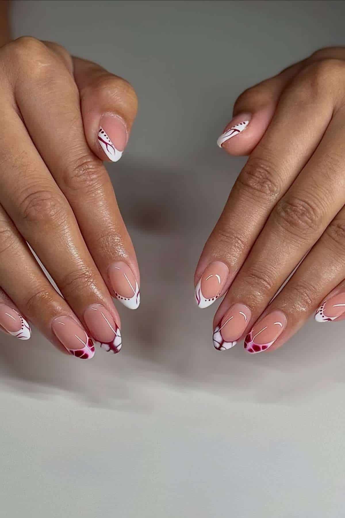 Hands with almond-shaped nails featuring a pink and white French tip design with red and white accent patterns.
