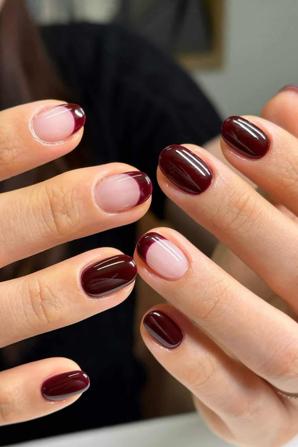 Hands with manicured nails featuring a combination of dark burgundy polish and French tips on a nude base.