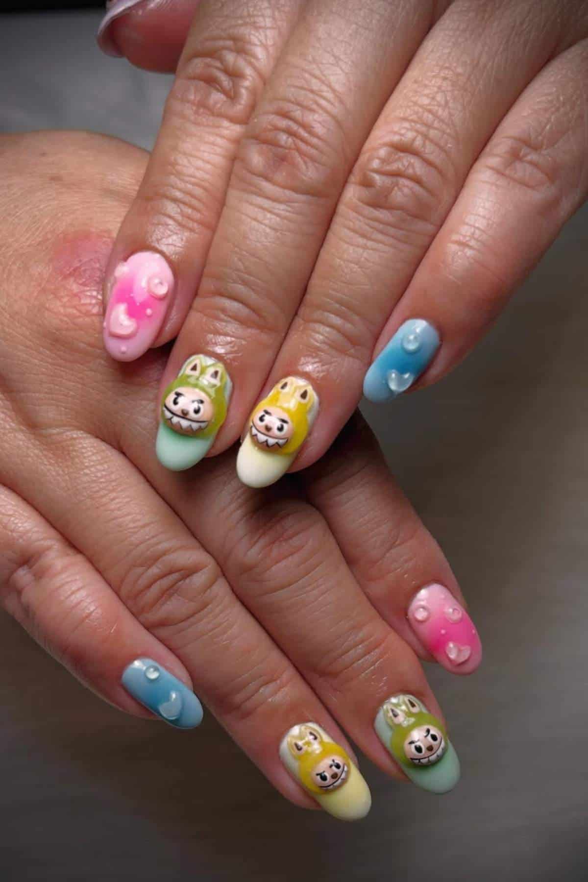Hands with pastel-colored nail art featuring 3D animal faces, pink hearts, and small pearl-like decorations on each fingernail.