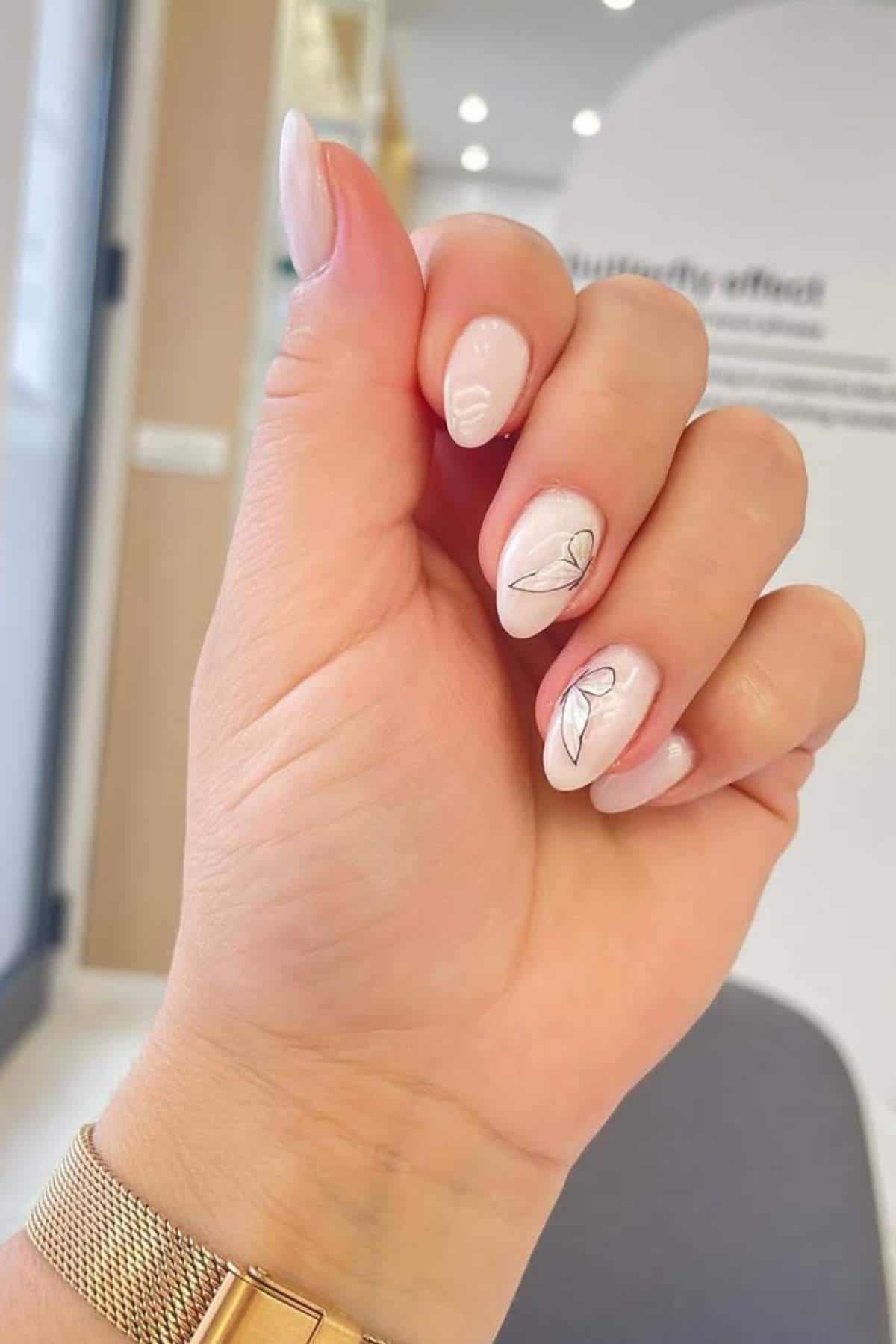 A hand with short, light pink nails featuring delicate black line art of leaves on two fingers, shown in a well-lit indoor setting.