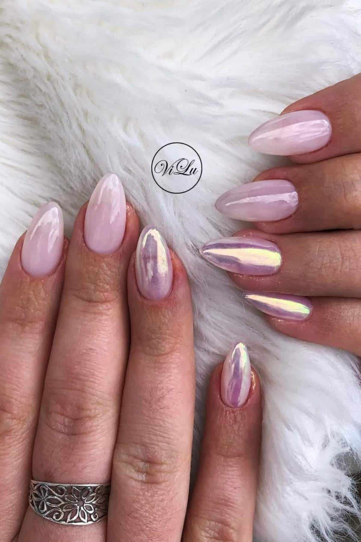Close-up of hands with almond-shaped nails featuring a glossy, iridescent pink and purple manicure, displayed on a white furry surface.