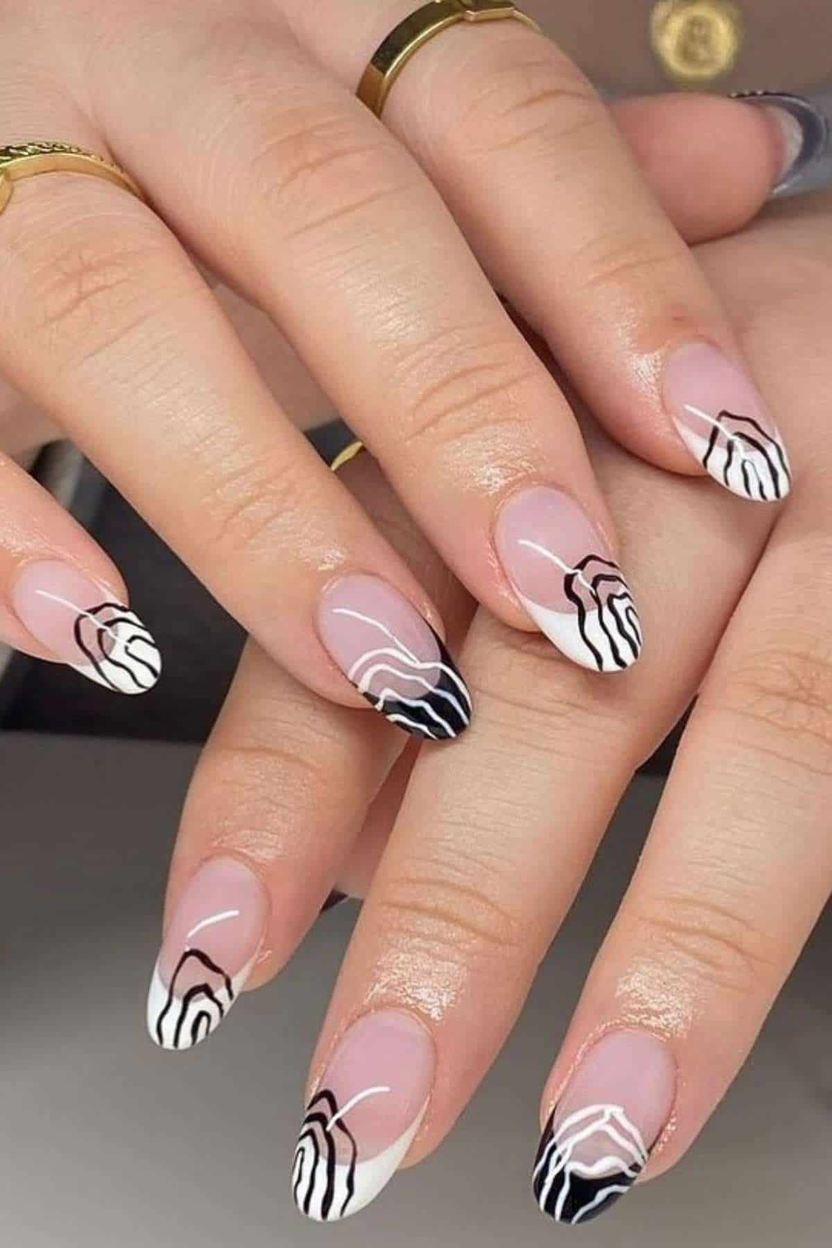 Close-up of hands with almond-shaped nails featuring abstract black and white line art designs on a nude base.