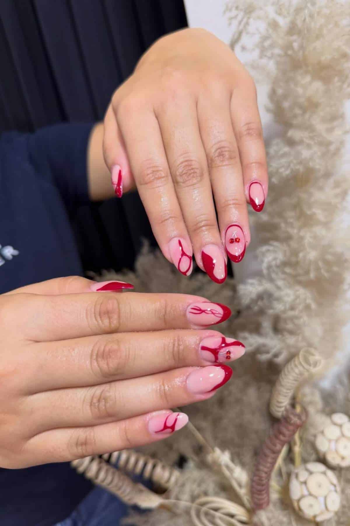 Close-up of hands with long almond-shaped nails featuring red and pink abstract nail art designs.