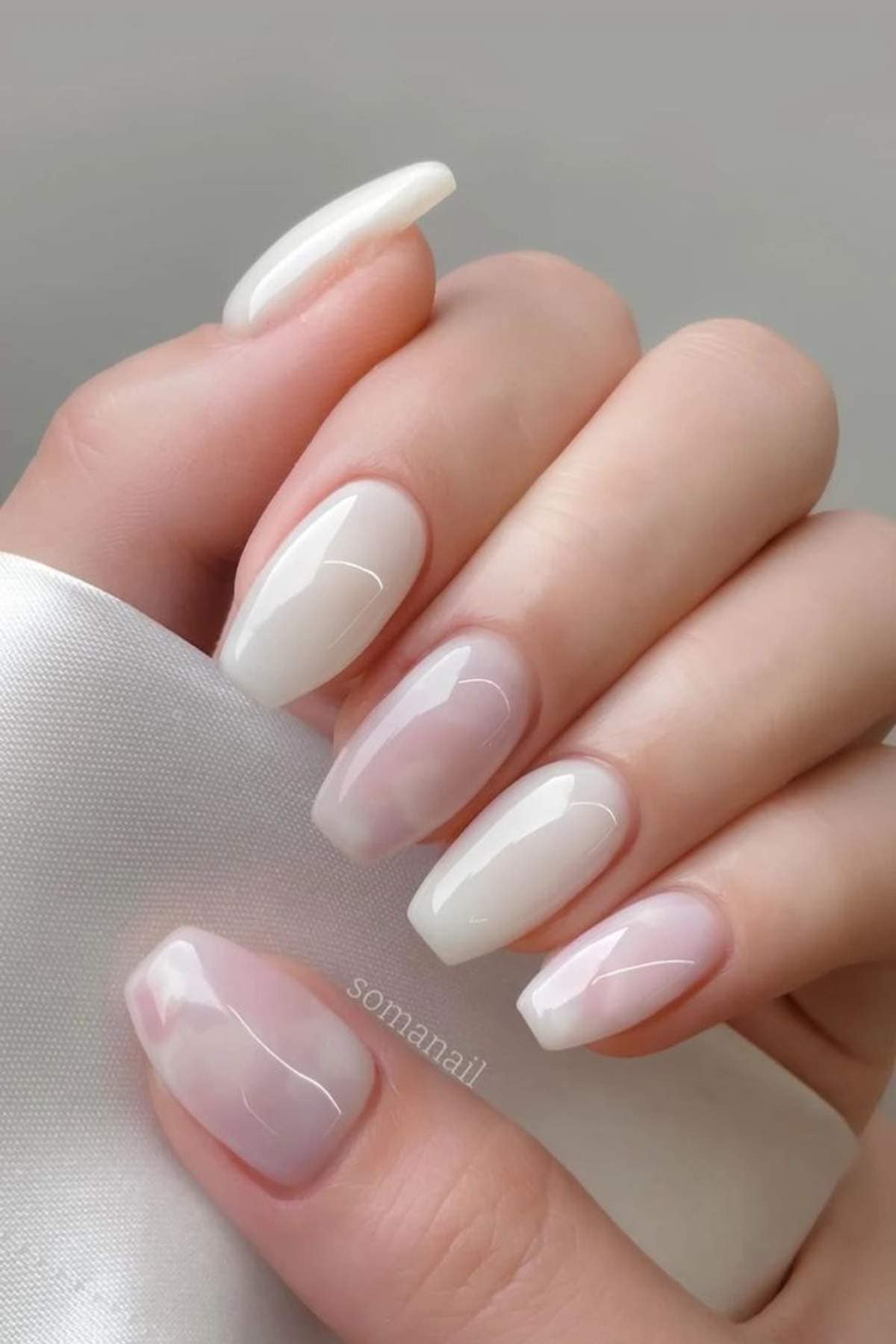 A hand with neatly manicured nails features a glossy, natural pink and white ombre design on medium-length almond-shaped nails.