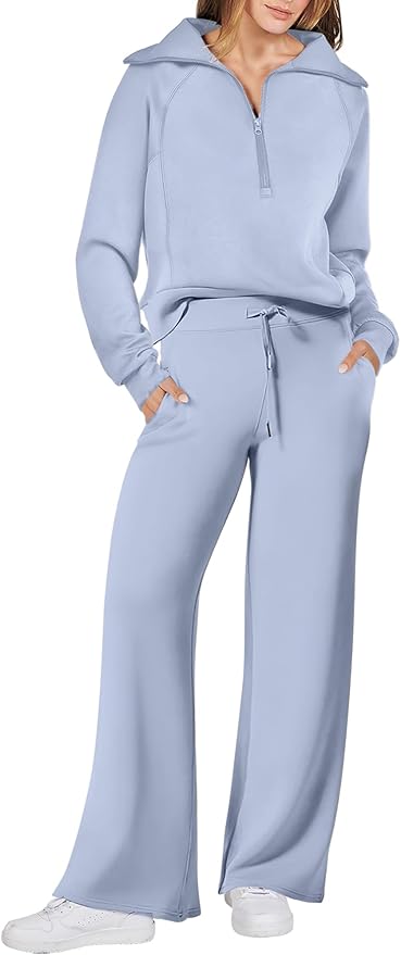 A woman is wearing a light blue zip-up collar sweatshirt and matching wide-leg pants with white sneakers.