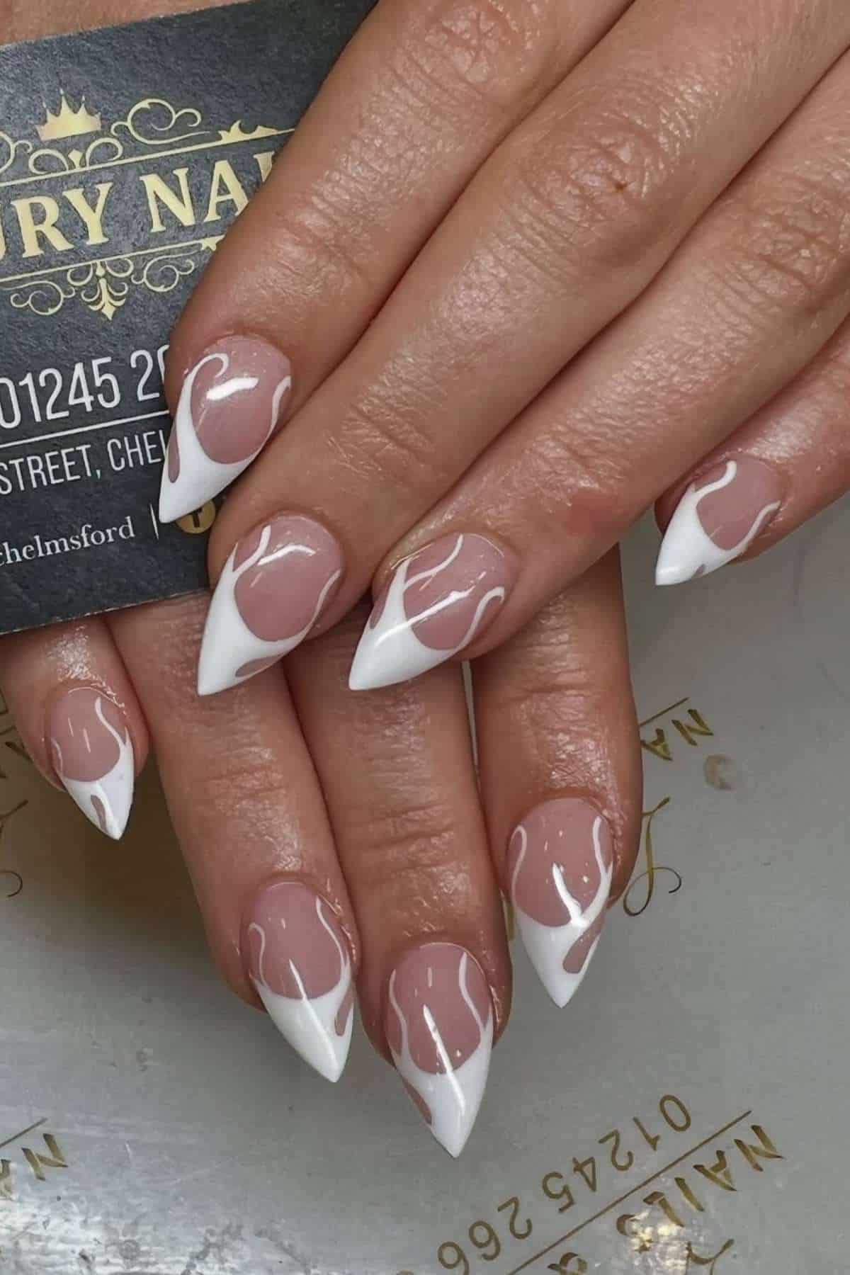 Hands showing long, almond-shaped nails with a French tip design and white swirl accents on a nude base.