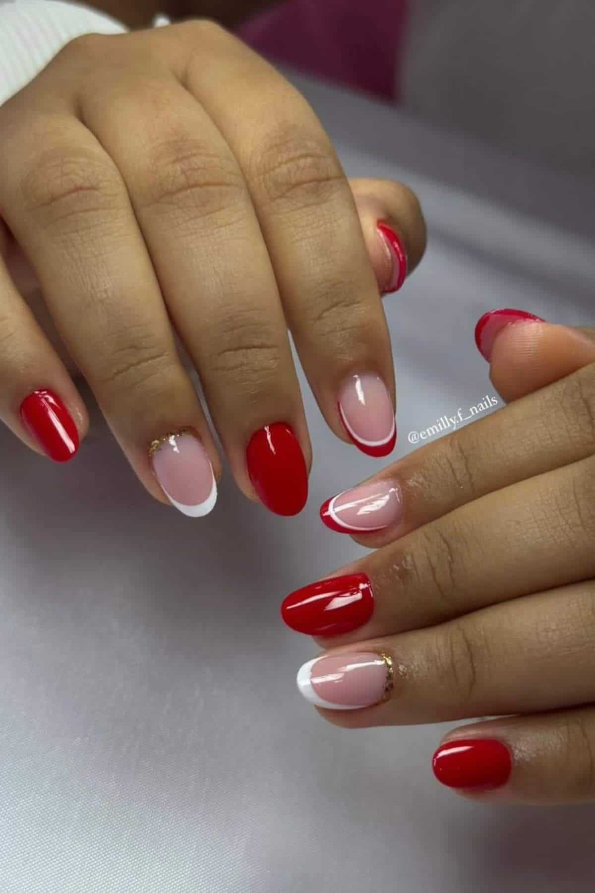 A person with manicured nails featuring red polish, pink nails with red and white tips, and gold accents, resting on a white surface.