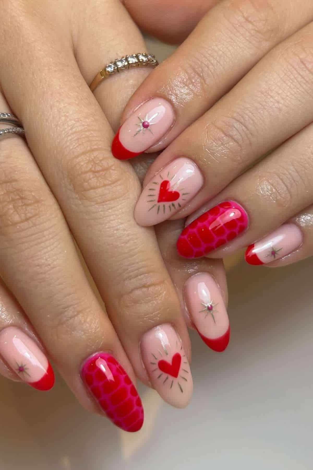 Hands with manicured nails featuring red French tips, heart designs, small star accents, and a textured red pattern on some nails.