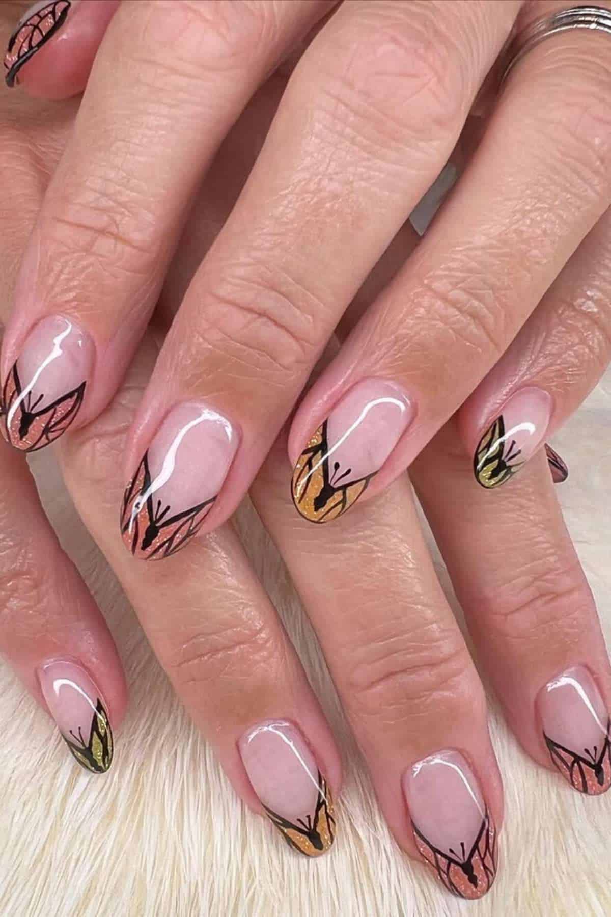 Close-up of hands with short, almond-shaped nails featuring nude polish and abstract leaf designs in black, gold, and green on each nail.