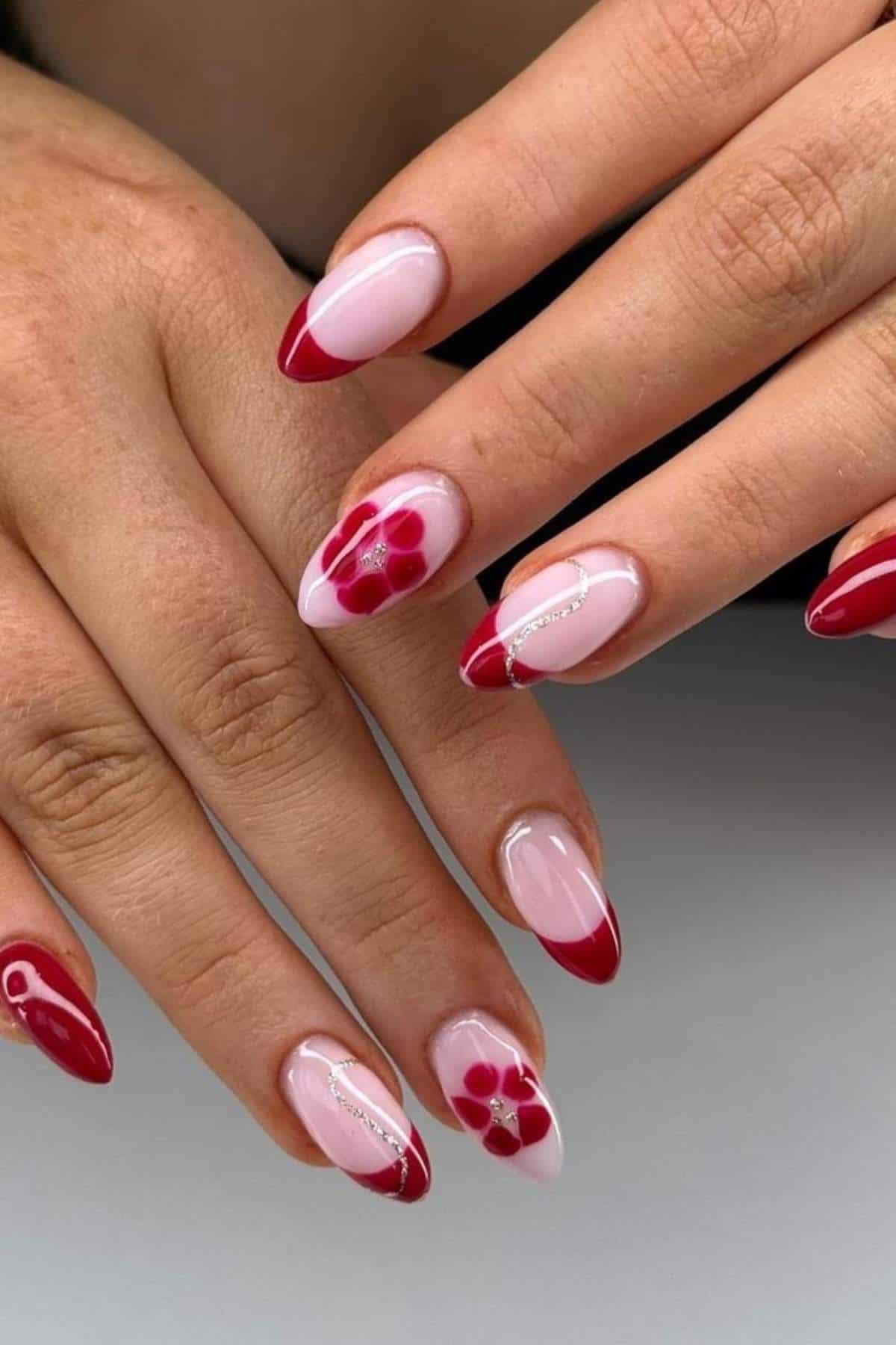 Hands with almond-shaped nails painted in light pink with red French tips, floral designs, and silver accents.