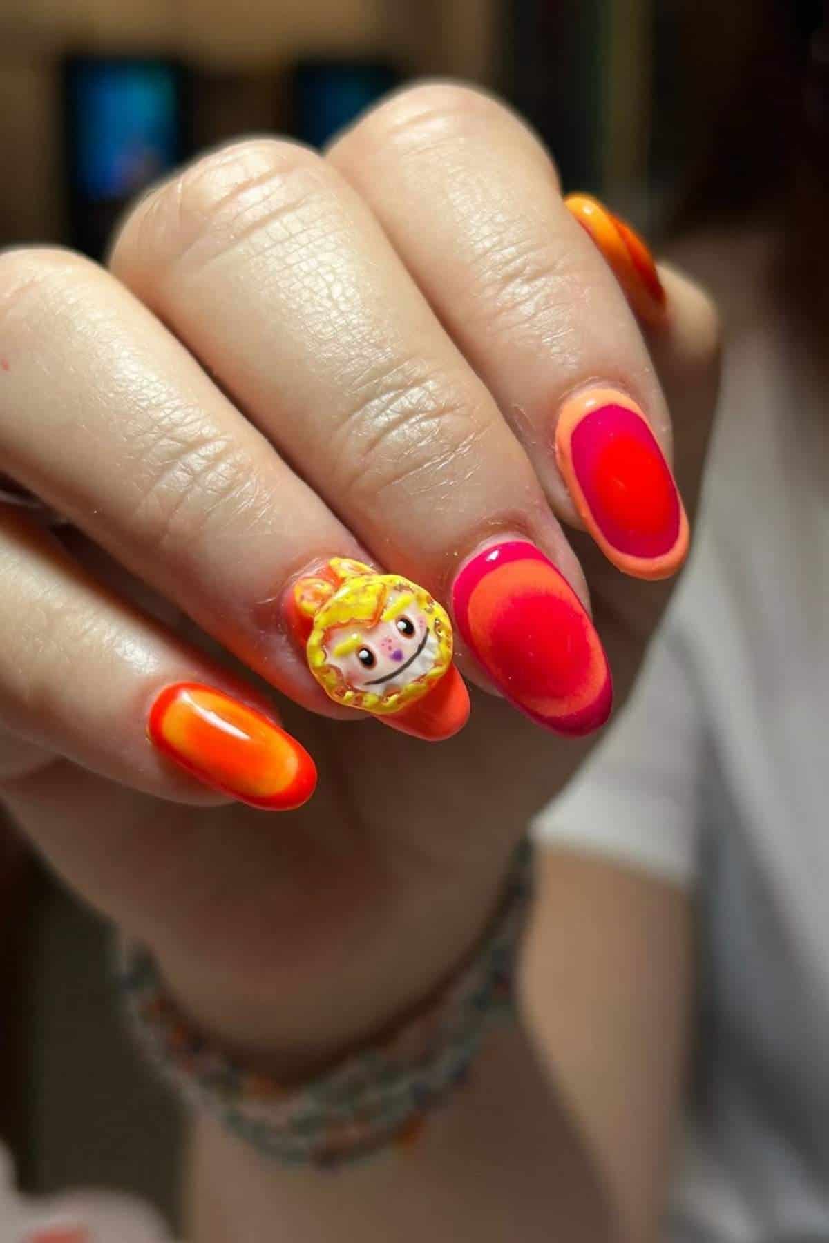 A hand with bright orange and red gradient nail polish; the ring fingernail features a 3D lion face design with a yellow mane.