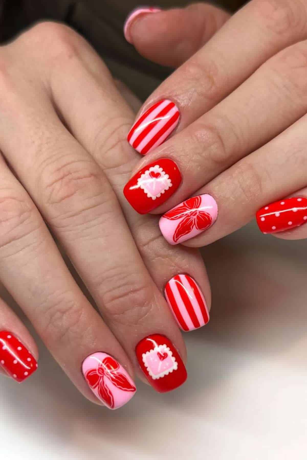 Fingernails painted with red, white, and pink nail art designs, including stripes, polka dots, hearts, and bows.