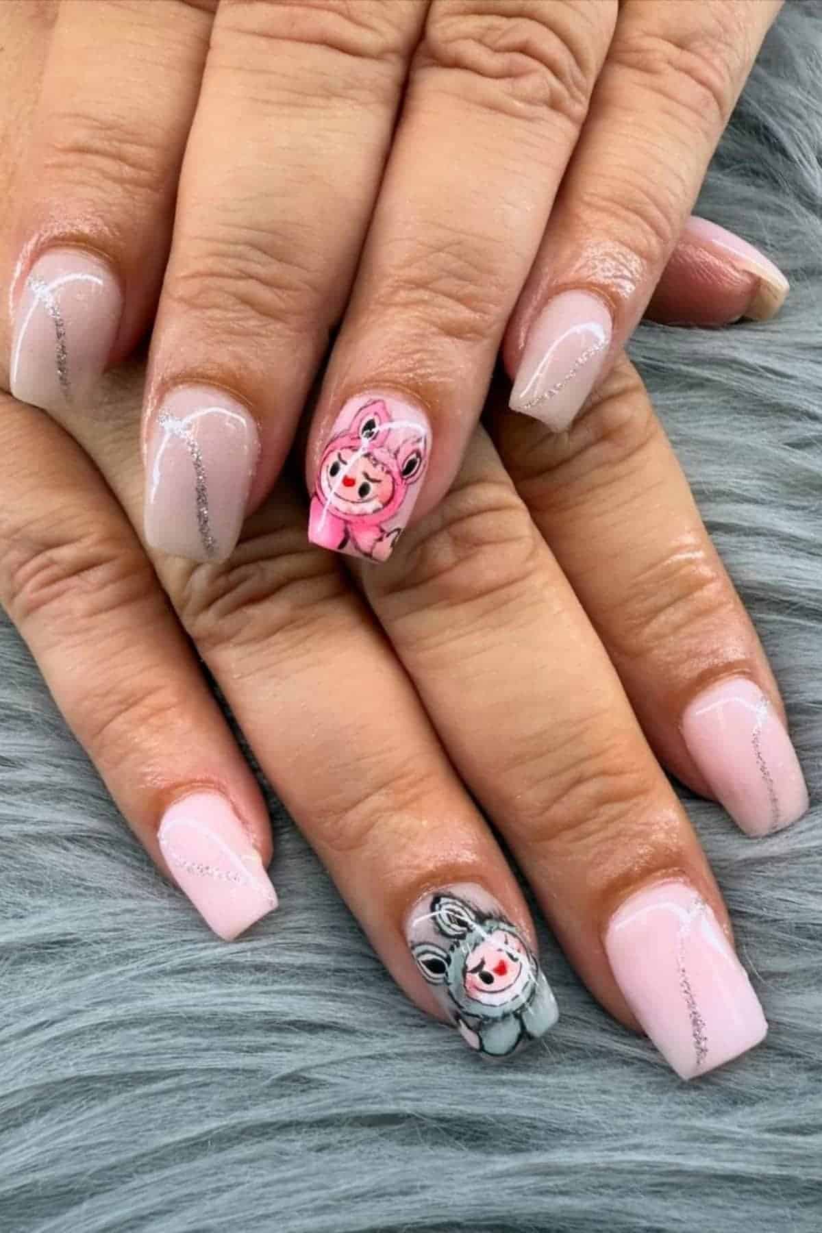 A hand with light pink manicure, featuring silver accent lines and cartoon pig and cow designs painted on the ring fingernails, resting on a gray textured surface.